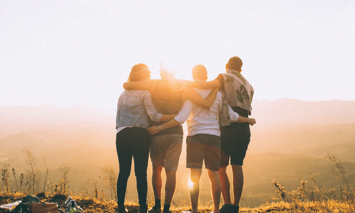 a group of 4 people seen from behind, holding each other looking at the sunrise